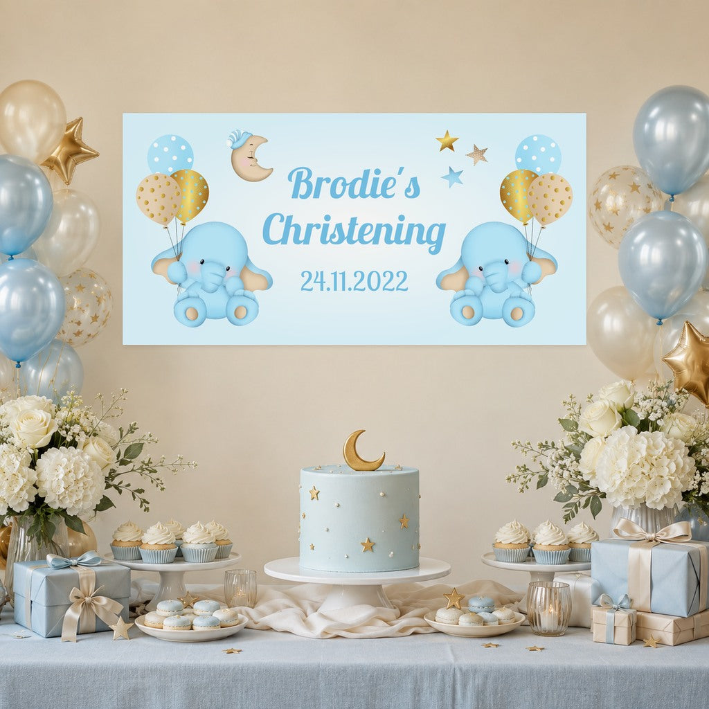 Blue and gold elephant christening decorations with Brodie's personalised banner, a pale blue moon and stars cake, cupcakes and balloons.