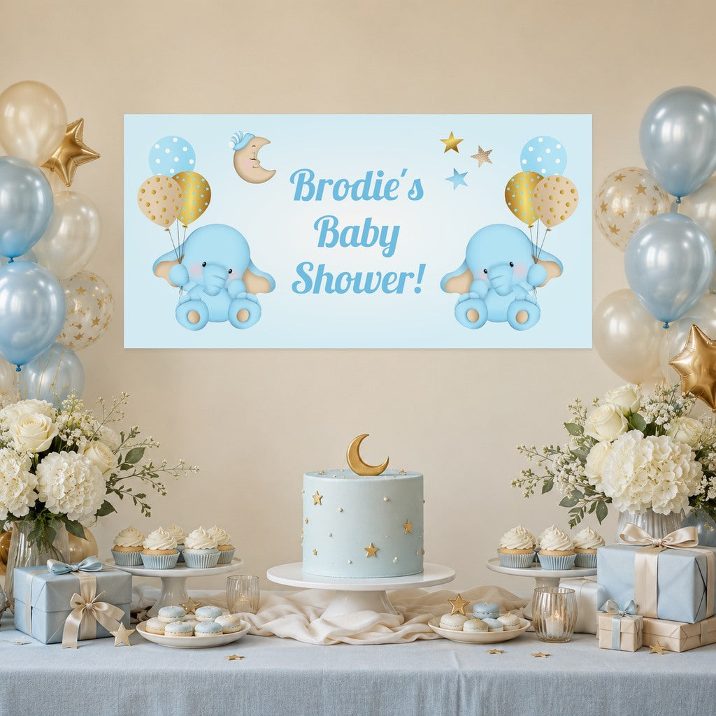 Blue and gold elephant baby shower decorations with Brodie's personalised banner, a pale blue moon and stars cake, cupcakes and balloons.