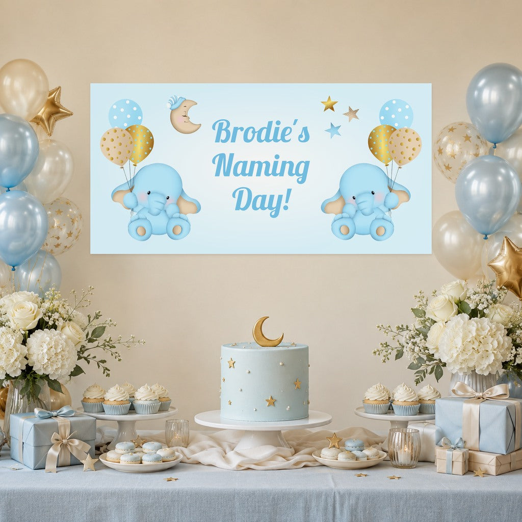 Blue and gold elephant naming day decorations with Brodie's personalised banner, a pale blue moon and stars cake, cupcakes and balloons.