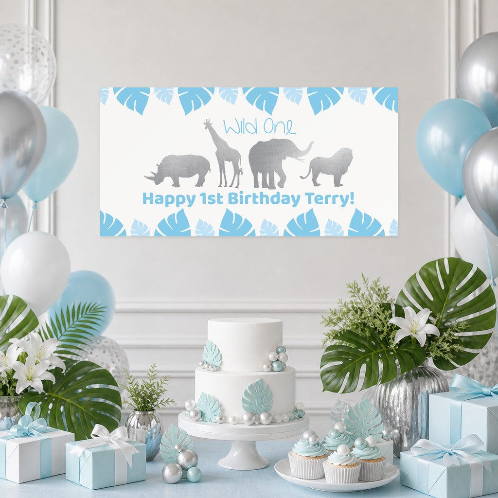 Blue Safari Wild One first birthday decorations with Terry's original personalised animal banner, a leaf-decorated cake, cupcakes, blue and silver balloons and matching gifts.