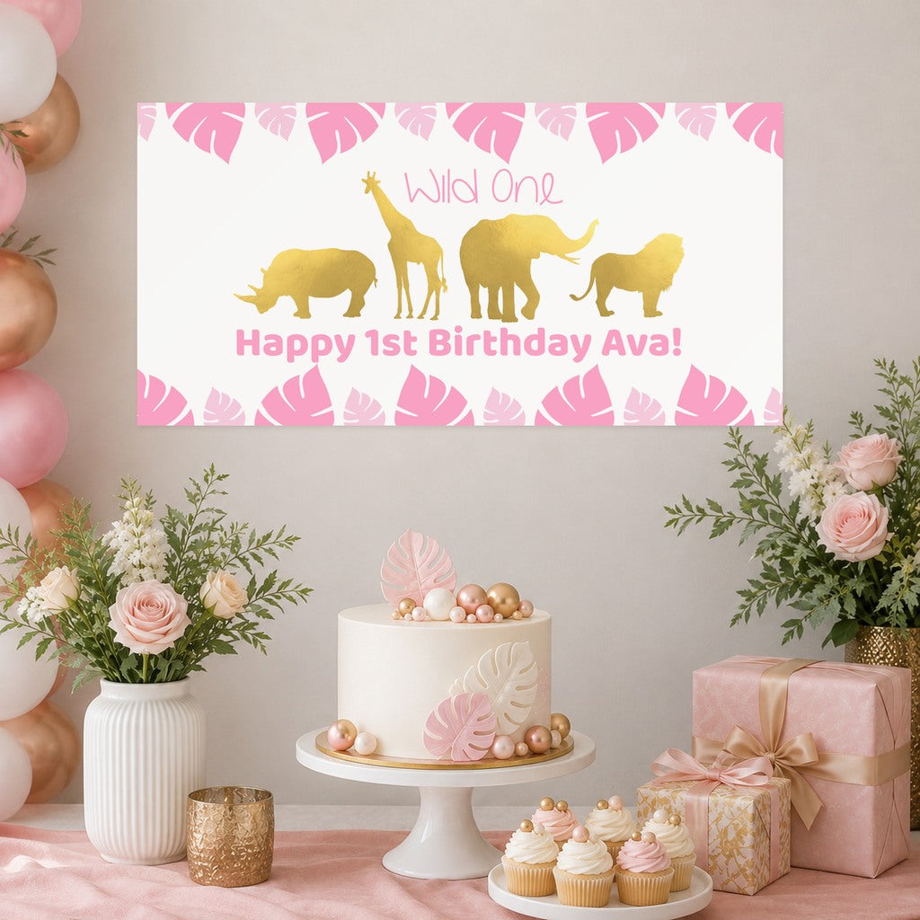 Pink Safari Wild One first birthday decorations with Ava's original personalised animal banner, a leaf-decorated cake, cupcakes, pink and gold balloons and matching gifts.