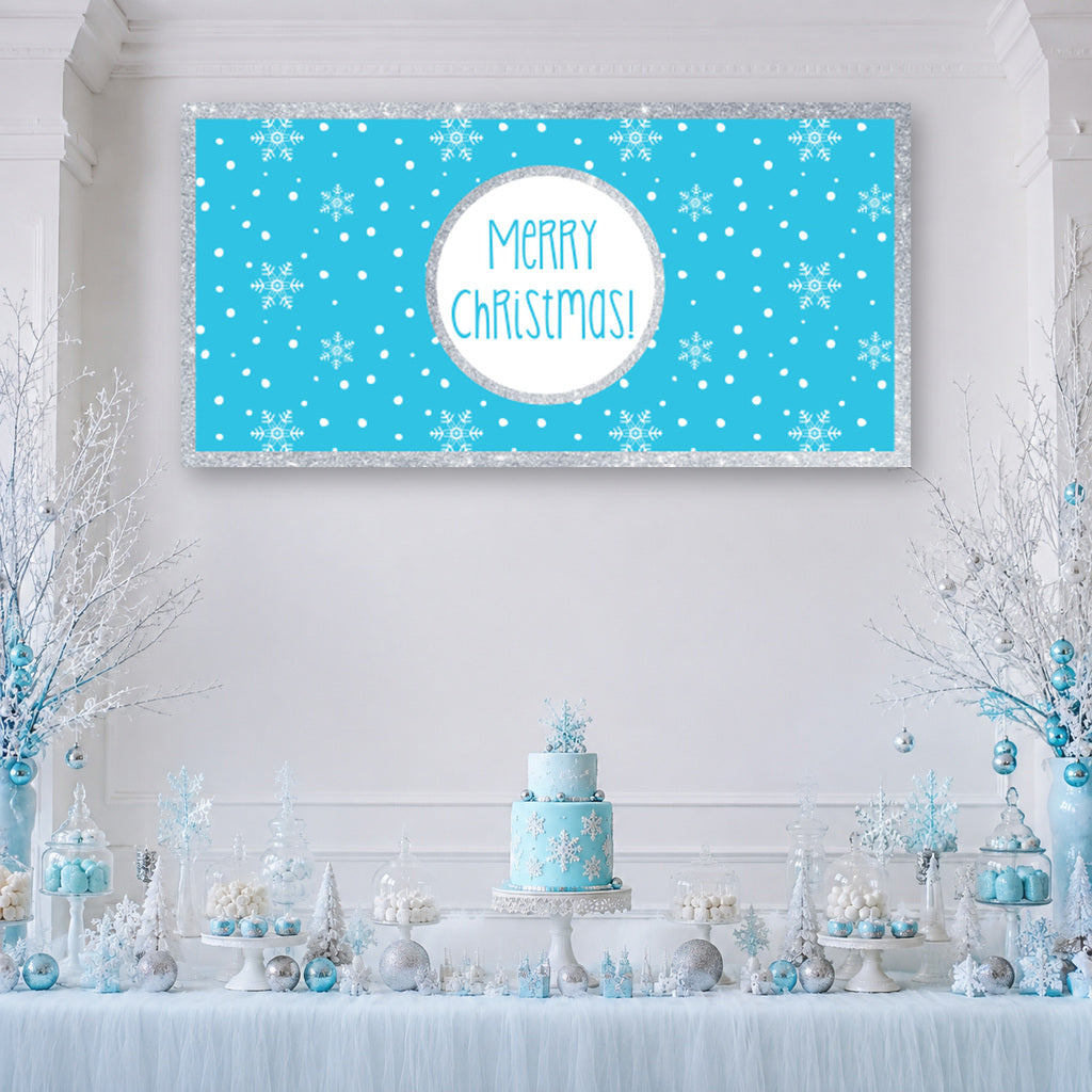 Winter Wonderland Christmas dessert table with a blue snowflake Merry Christmas banner, blue and white cake, silver trees and decorations.
