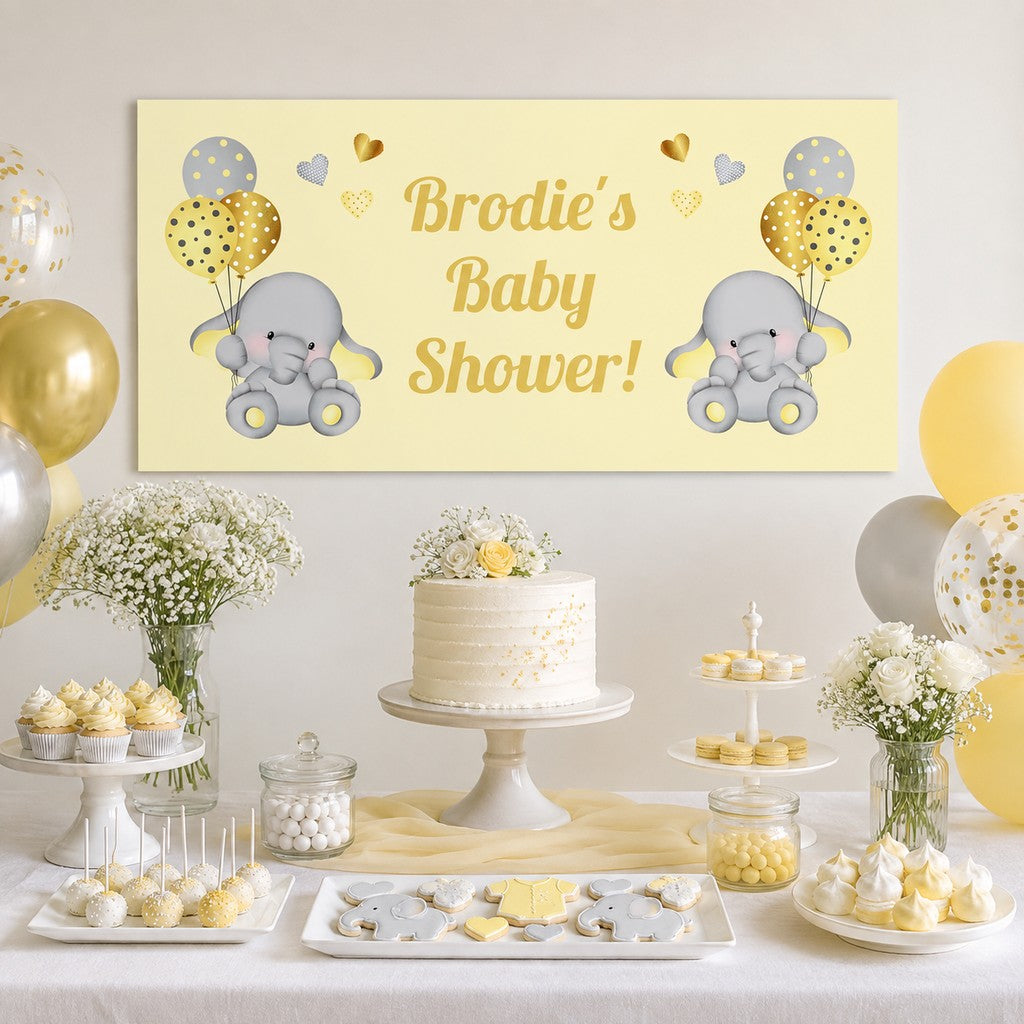 Yellow elephant baby shower dessert table with Brodie's personalised banner, cake, balloons and matching blue and yellow party decorations.