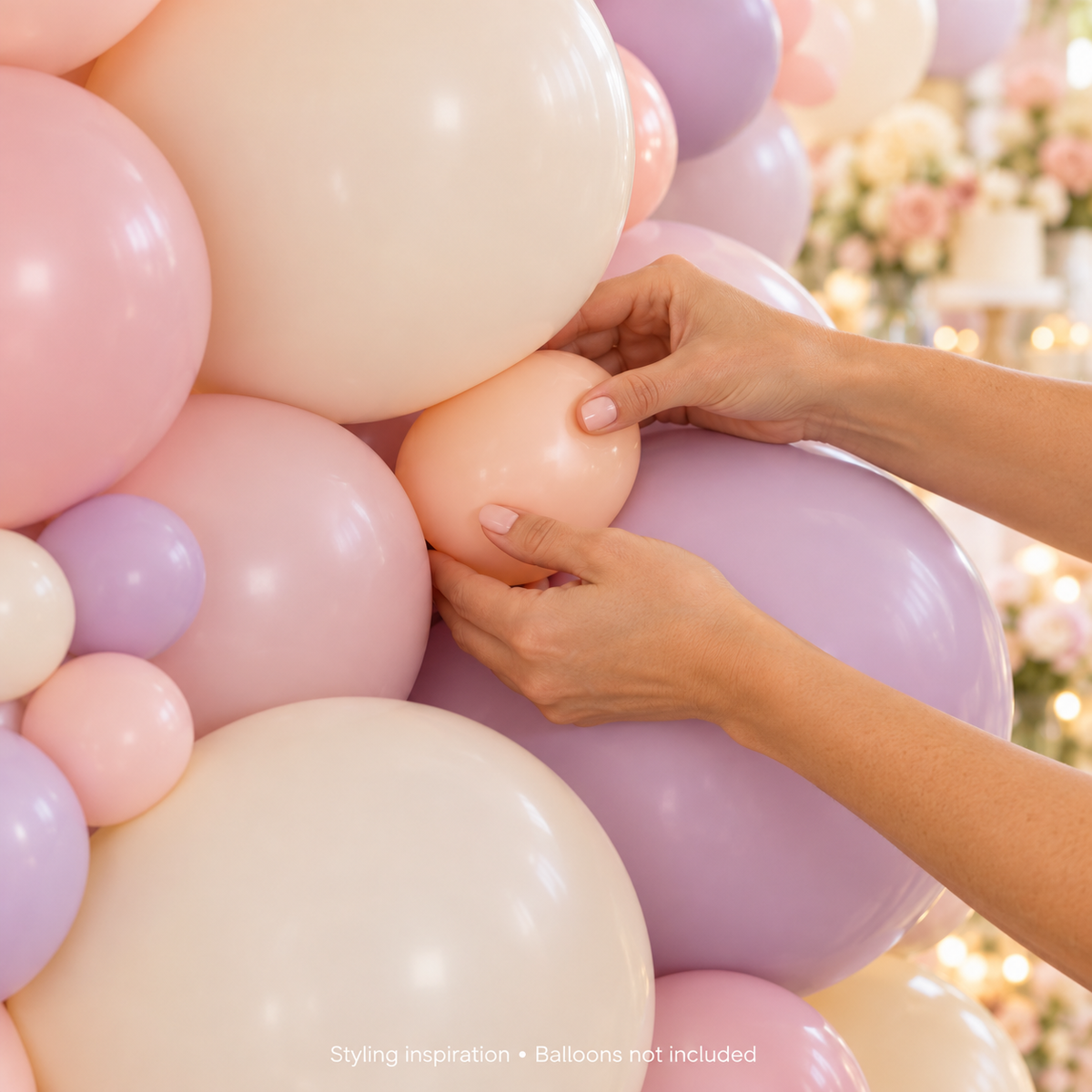 Hands adding a small peach balloon to fill a gap in a pastel garland; balloons not included
