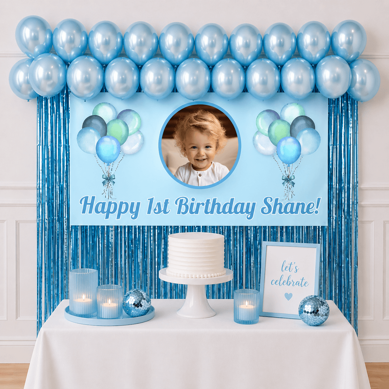 Personalised pastel blue celebration party package with photo banner, pearl blue balloons and blue foil fringe curtains displayed as a completed party setup