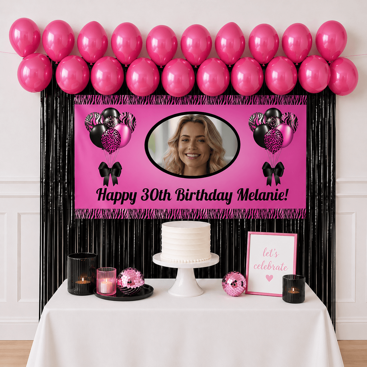Personalised pink and black celebration party package with photo banner, hot pink balloons and black foil fringe curtains displayed as a completed party setup