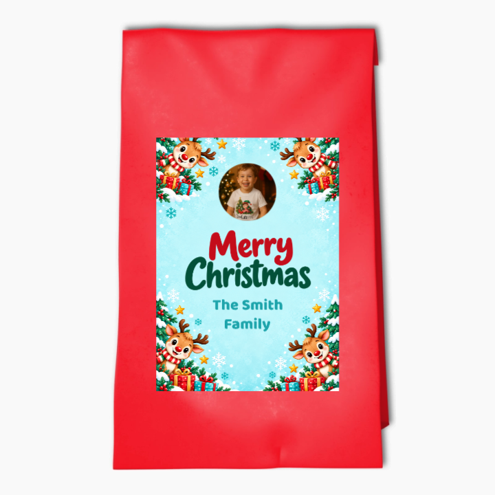 Red Rudolph Christmas party bag with a personalised photo label, family name, reindeer and presents on a snowy blue background.